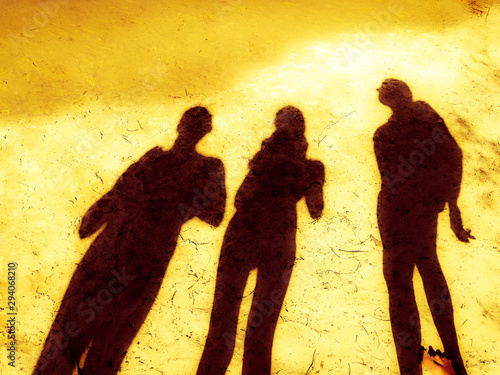 three shadows of people on a sunny sandy beach, yellow blurred background