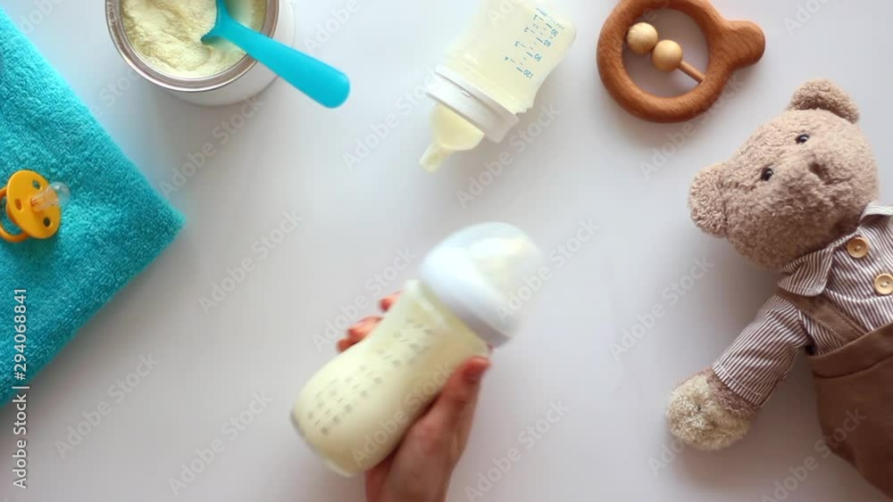 Hand holding the baby bottle with milk on white table with toys. Top view Hand holding the baby bottle with milk on white table with toys. Top view