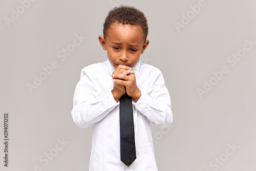 Fotografía Portrait of nervous frustrated sad African American schoolboy in uniform looking down with worried facial expression, gnawing nails, scared of being told off for bad marks at school