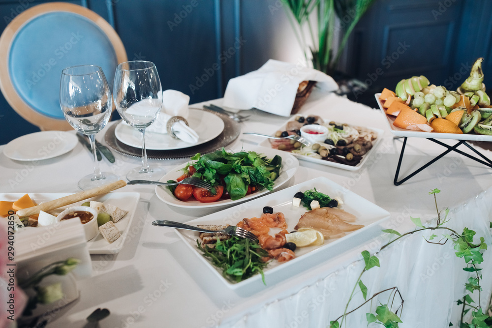 Wedding table with white tablecloth served with healthy greens, cold fish platter, cheese platter and fruit platter. Wedding table with white tablecloth served with healthy greens, cold fish platter, cheese platter and fruit platter.