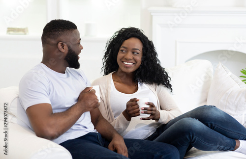 Happy black couple relaxing on couch and drinking coffee