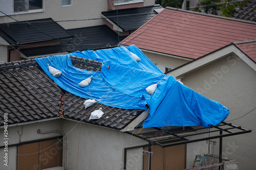 Fotografi Tattered blue tarp on roof after strong typhoon wind damage