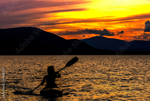 Silhouette kayaking at sunset, lake and mountains background