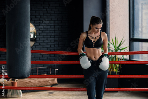 Attractive sports caucasian girl leaned on the ropes on boxing ring, have a rest after intensive workout in modern loft gym. photo