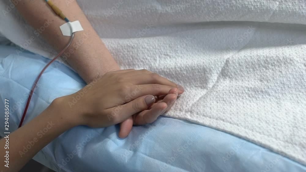 Relative holding ill woman by hand in hospital ward, support in sickness Relative holding ill woman by hand in hospital ward, support in sickness