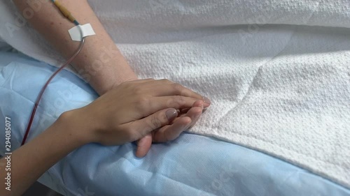 Relative holding ill woman by hand in hospital ward, support in sickness