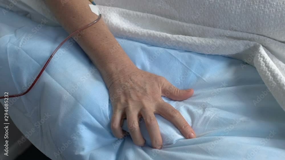 Hand of sick senior patient squeezing bed sheet in hospital, suffering pain Hand of sick senior patient squeezing bed sheet in hospital, suffering pain