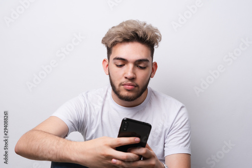 chico joven concentrado mirando su celular en una pared blanca © Yoshi