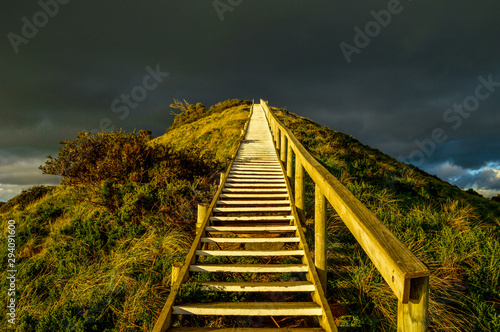 Obraz na plátně Steep golden staircase going up a hill with dark clouds in the background