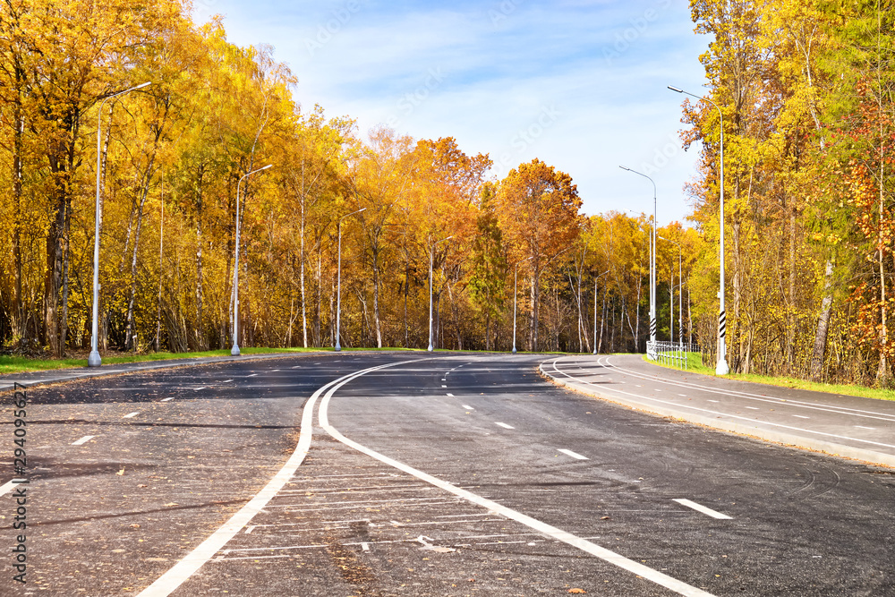 Obraz premium golden autumn road forest landscape on sunny day against blue sky background street view of new modern 4 lane freeway with pedestrian and bike path and light poles in moscow russia