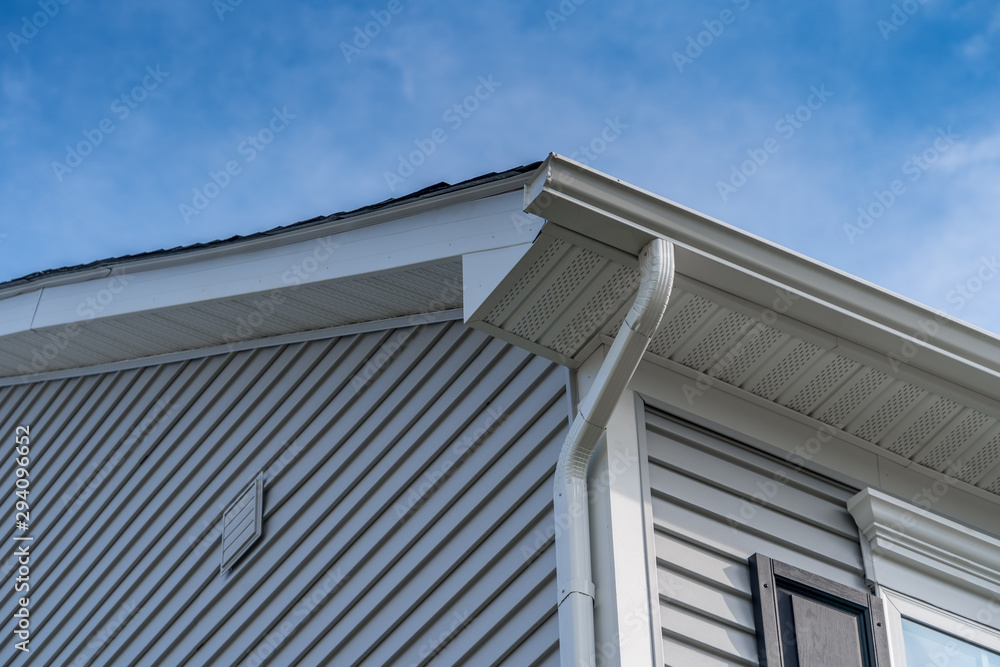 Gable with gray horizontal vinyl siding, white frame gutter guard system, fascia, drip edge, soffit, on a pitched roof attic at a luxury American single family home neighborhood USA