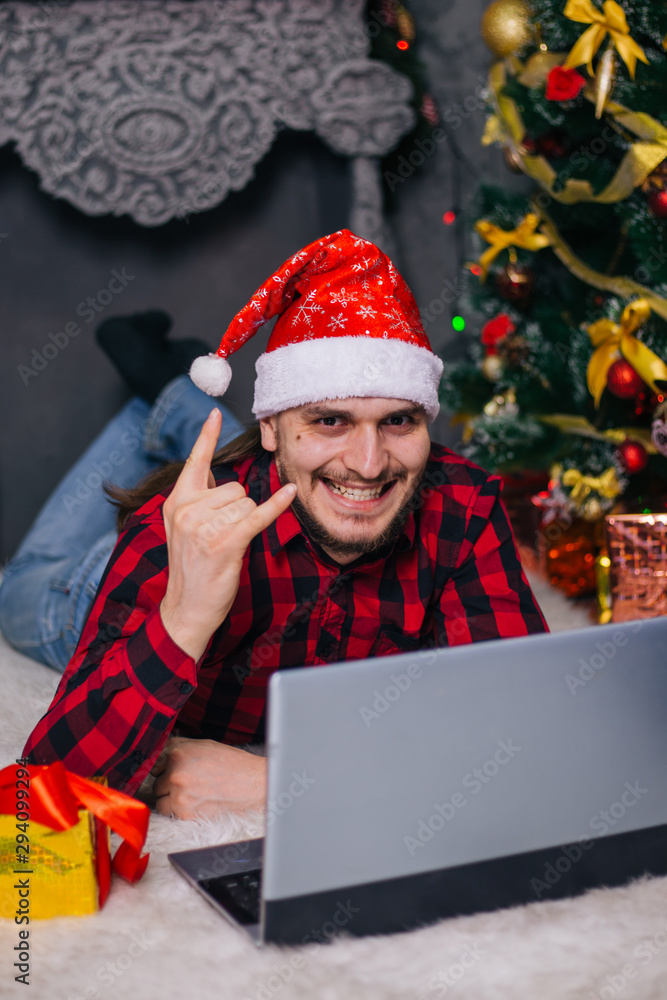 The guy in the red Santa hat is lying on the carpet near the fireplace. A man with a laptop. The guy in the red Santa hat is lying on the carpet near the fireplace. A man with a laptop.