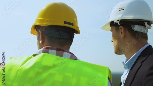 Contractor and male customer in helmets discussing future building place on roof