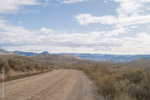 Dirt road in the rural part of Kamloops, BC, Canada. Lac Du Bois Grasslands, vast open space with fields, hills, forested mountains, desert like landscape