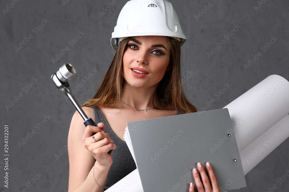 Young beautiful brunette girl wearing white helmet portrait over grey background. Manual job DIY inspiration improvement fix wrench startup instrument pad industrial profession career tool help