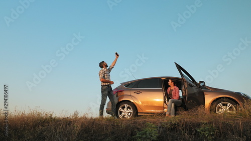 Man and woman traveling by car catches a phone signal while standing on the side of the road
