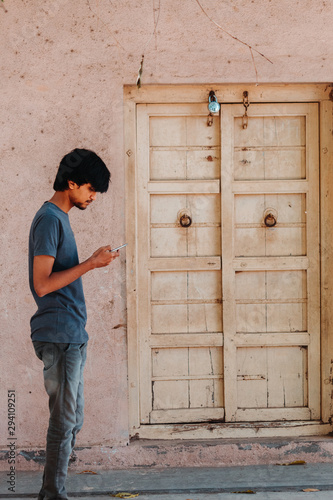 Indian male model using mobile phone besides the wooden door