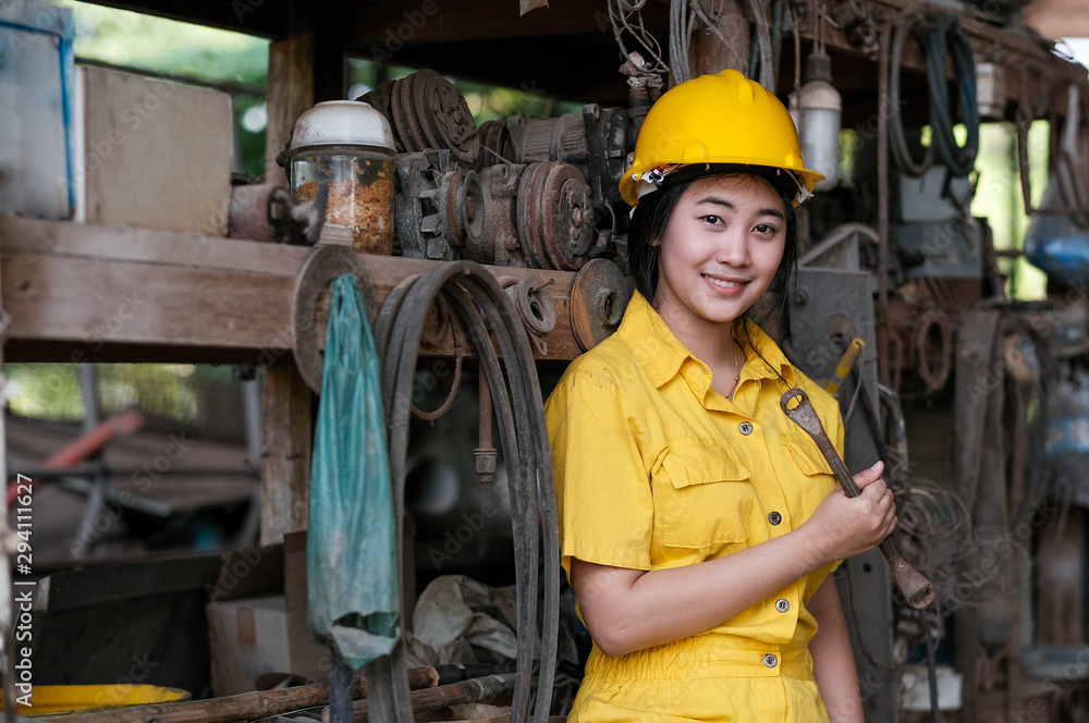 Asian pretty technician girl hold old wrench and stand in front of shelves with a lot of tools and instruments. Asian pretty technician girl hold old wrench and stand in front of shelves with a lot of tools and instruments.