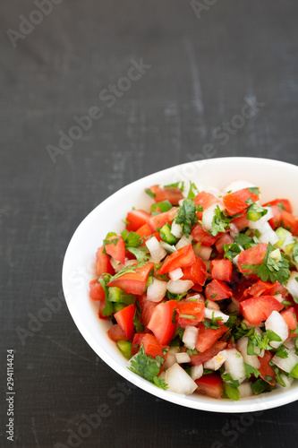 Pico de Gallo in a white bowl on a black surface, low angle view. Space for text.