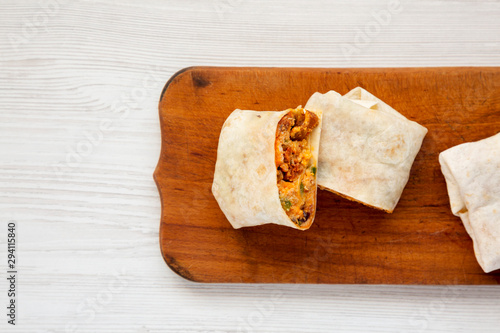 Homemade chorizo breakfast burritos on a rustic wooden board on a white wooden surface, overhead view. Flat lay, from above, top view. Copy space.
