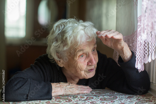 Old gray-headed woman sits in a house near the window.