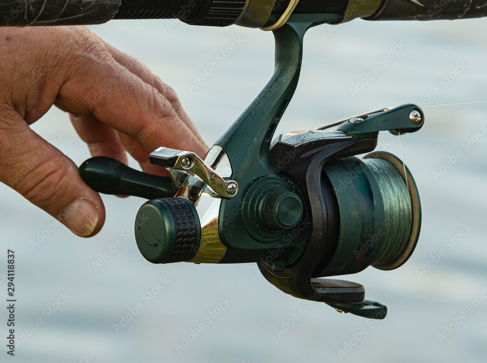 spinning fishing reel and fishing rod fishing on the river close up man twists hands spinning fishing reel and fishing rod fishing on the river close up man twists hands