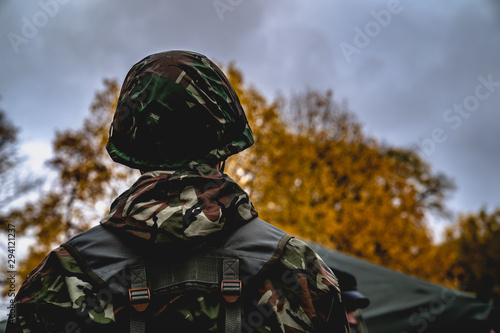 Soldier in the uniform. Back view. Low angle. Cloudy weather, autumn. Military concept. Yellow tree on the background © Dmitrii