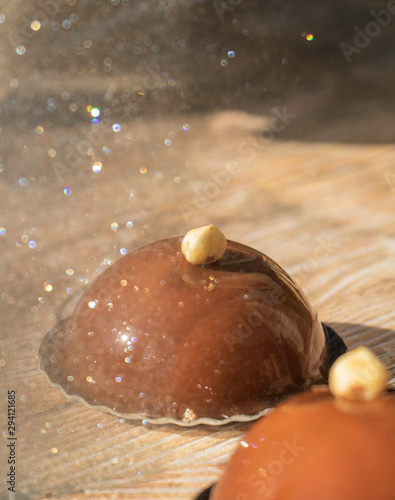 Reflet d'un gâteau Opéra au chocolat et praliné en forme de dôme avec une noisette dans un miroir à paillettes avec un fond bois