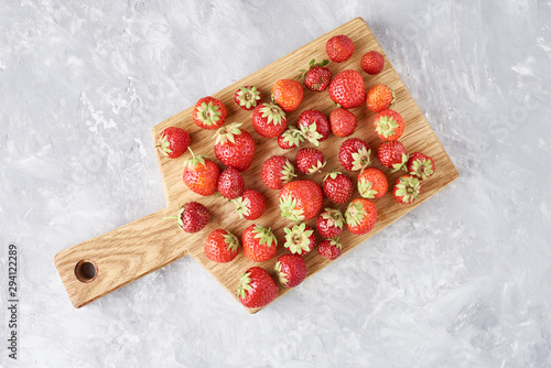 Heap of fresh strawberries with cutting board on a gray background, top view. Healthy nutrition