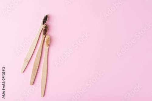 three wooden bamboo toothbrushes on a pink background  top view.  Dental care concept