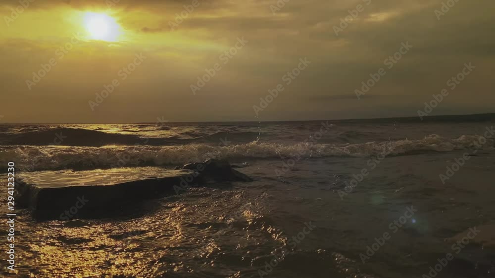 SLOW MOTION. Sun rays emerging through clouds in the middle of the rough exotic sea. Breathtaking view of tropical shore. Waves crashing onshore, shiny wet stones at sunset with mountain landscape SLOW MOTION. Sun rays emerging through clouds in the middle of the rough exotic sea. Breathtaking view of tropical shore. Waves crashing onshore, shiny wet stones at sunset with mountain landscape