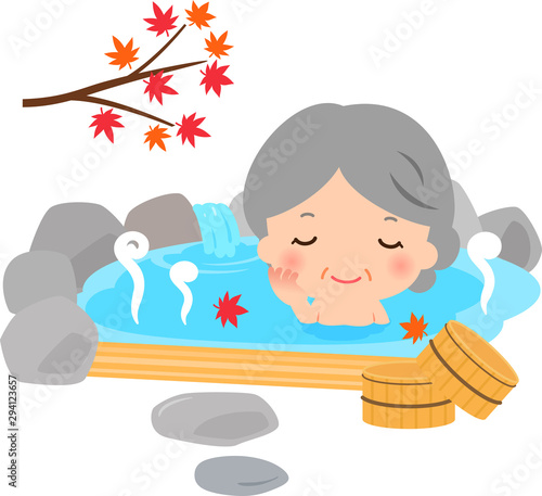 紅葉の下の露天風呂に入る笑顔のシニア女性