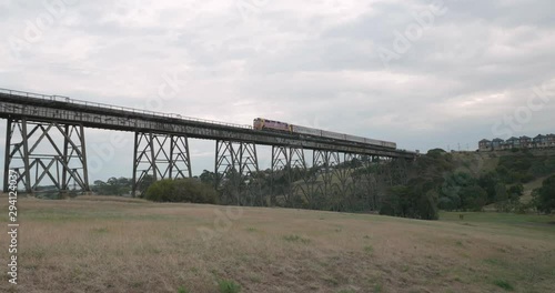 Follow view of a train crossing a old historic narrow trestle railway bridge from a field below the bridge photo