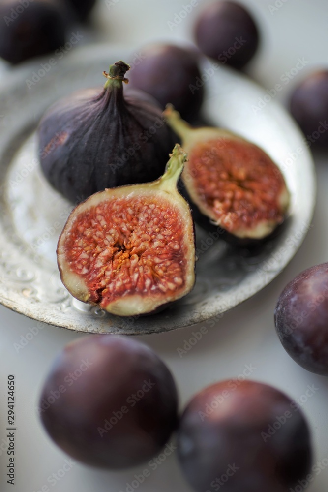 Ripe violet figs, cut in half and whole in vintage silver plate and on a white table around. Selective art focus. Ripe violet figs, cut in half and whole in vintage silver plate and on a white table around. Selective art focus.