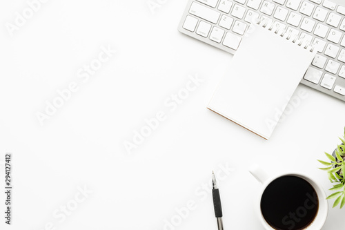 White office desk table with blank notebook page with pen, cup of coffee and small plant pot. Top view with copy space, flat lay.