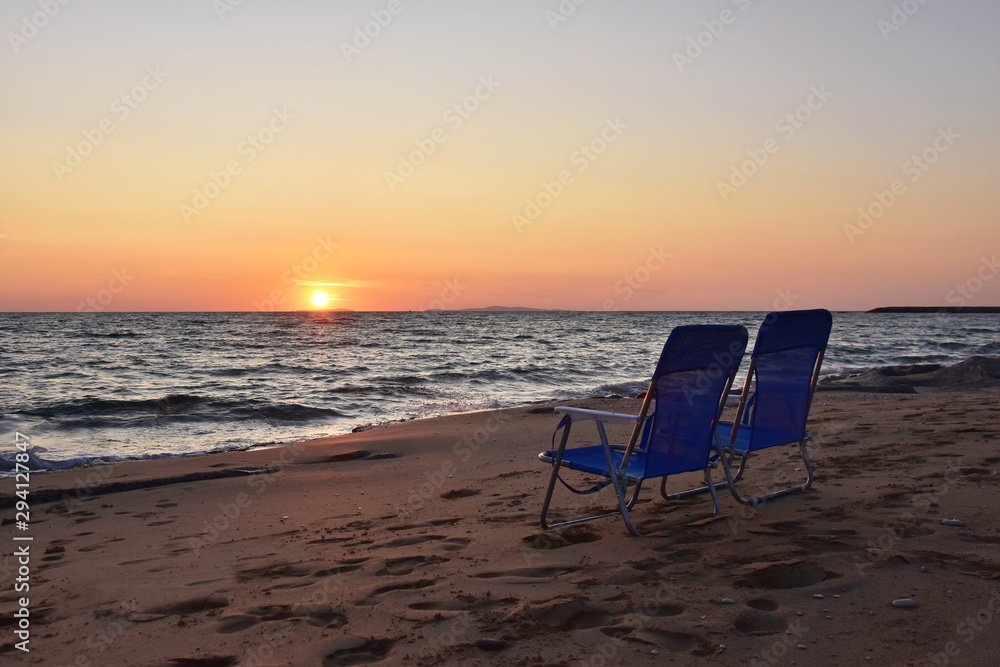Looking to the sea two empty chairs on sandy beach at sunset; Ionian coast, Greece
