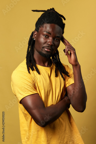 Portrait of handsome African American man keeping his fingers on his temple isolated on yellow background, let me think. close up photo, people, fashion, fist think, than do