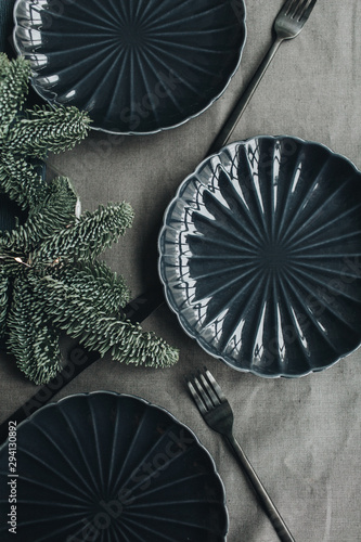 Christmas / New Year composition. Festive christmas / Thanksgiving table decorated with fir branches, garland, dark blue plates, black knifes and forks. Flat lay, top view. Winter holidays concept.