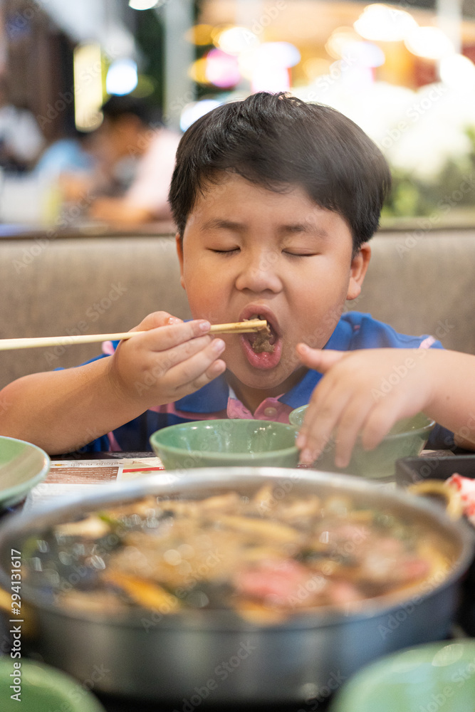 A kid is eating deliciously boiled beef with sukiyaki soup in a shabu pot at the Japanese restaurant. A kid is eating deliciously boiled beef with sukiyaki soup in a shabu pot at the Japanese restaurant.