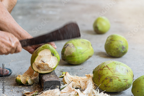 Green fresh coconut peeling and shelling with heavy chop knife for juice.