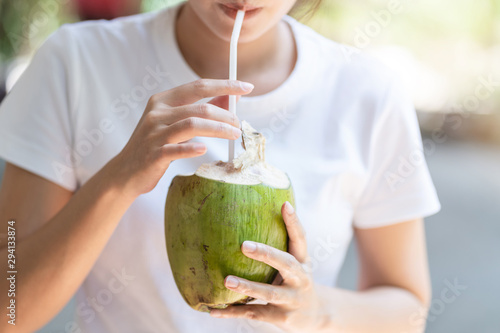 Young Asian woman tourist holding green coconut and drinking fresh coconut water.