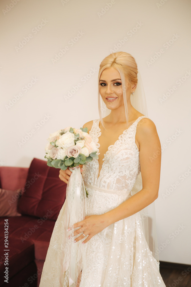 Elegant bride in beautiful wedding dress with bouquet at home. Blond hair woman with beautiful makeup and hairstyle Elegant bride in beautiful wedding dress with bouquet at home. Blond hair woman with beautiful makeup and hairstyle