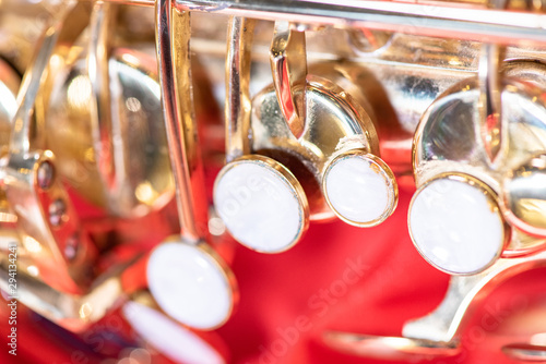 Beautiful macro photo of the details of a wind instrument of a golden alto saxophone on a red background