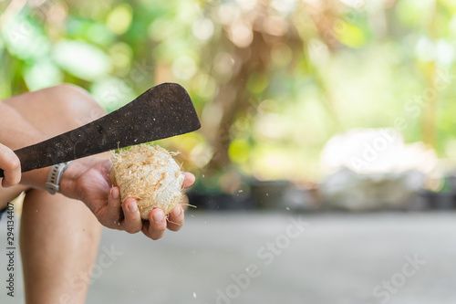 Green fresh coconut peeling and shelling with heavy chop knife for juice.