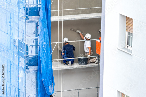 trabajadores pintando una fachada sobre un andamio