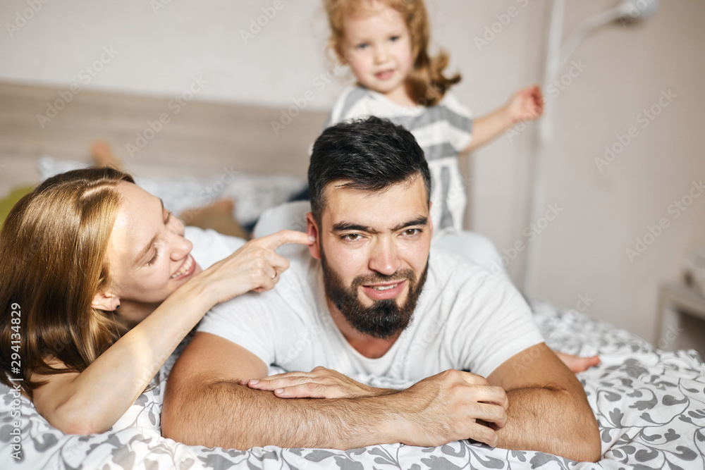 cheerful bearded man lying on the bed, blonde woman touching her husband's ear. close up photo