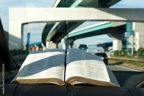 Open Holy Bible inside the car. Background blurred with motorway junction in Tomei Expressway, Japan. Close-up. Horizontal shot. © Sergio Yoneda