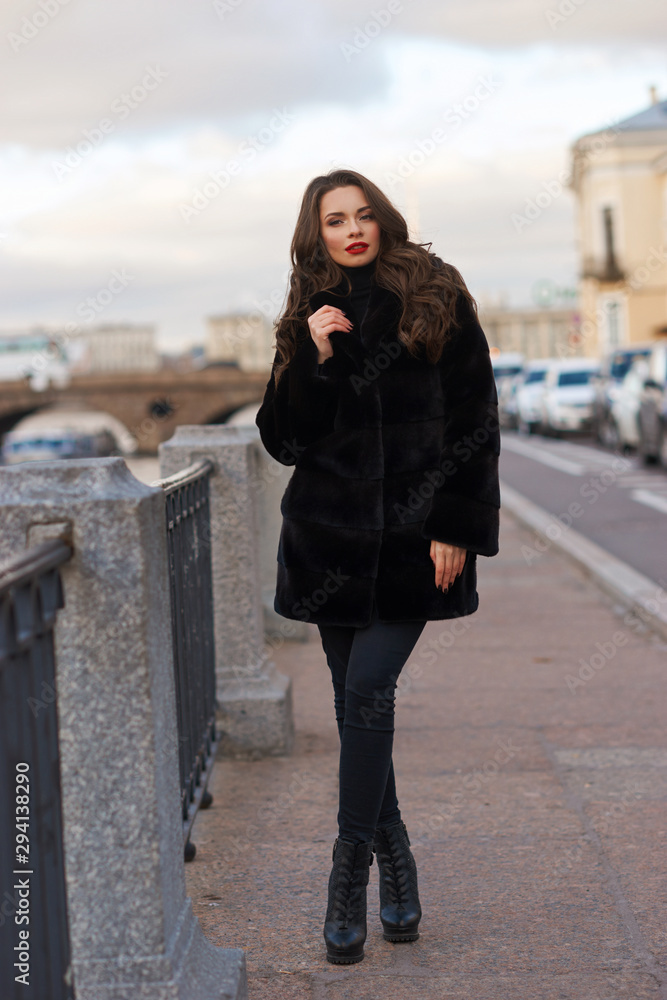 Young beautiful female model in black fur coat with long dark wavy hair. Outdoor portrait