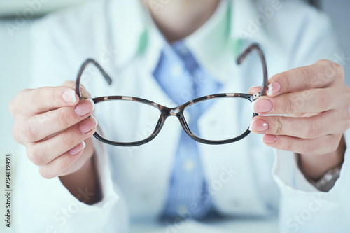 Female optician hands giving new glasses to customer for testing and trying close-up. Eye doctor with client comparing spectacles and choosing lenses in store.