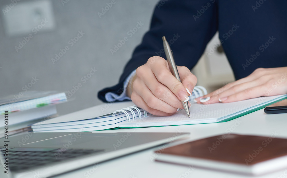 Young businesswoman writing in notepad while sitting at the office. Female hands holding a pen and making notes close up. Young businesswoman writing in notepad while sitting at the office. Female hands holding a pen and making notes close up.
